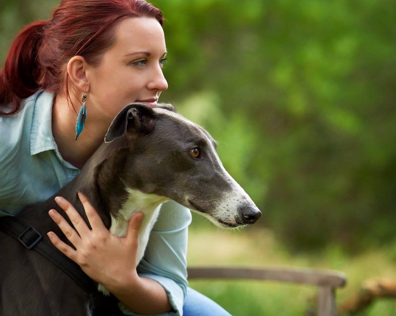 Photograph of artist Sarah embracing her grey greyhound in a leafy garden
